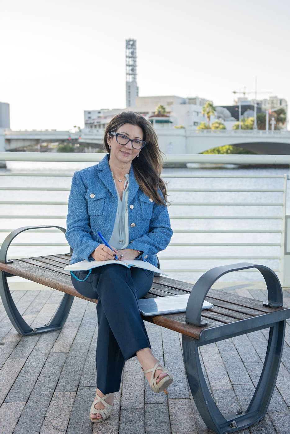 Carrie writing in a notebook on a bench by the river
