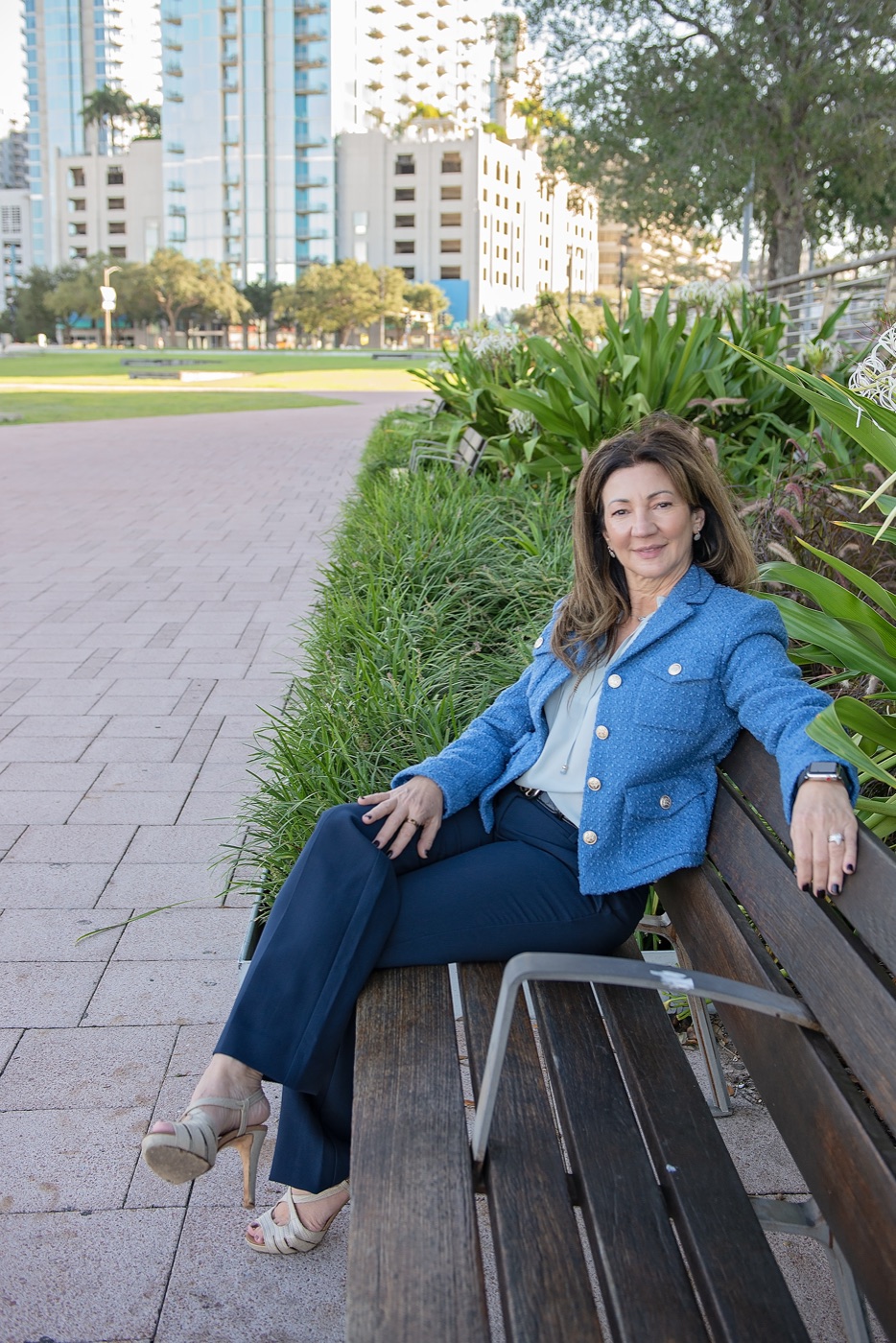 Carrie sitting on a riverside bench in a blue jacket, smiling
