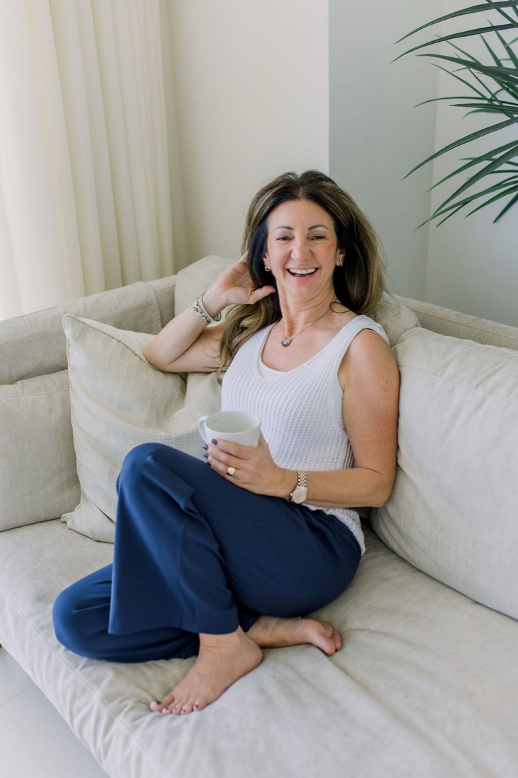 Carrie laughing on a white sofa in a bright living room