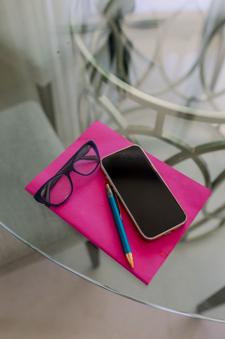 A pink notebook, glasses and a phone on a glass table
