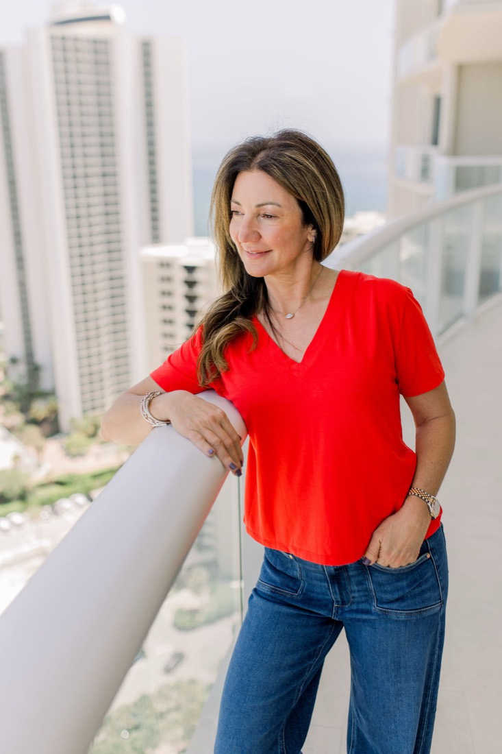 Carrie in a red top leaning on a balcony railing high above the water